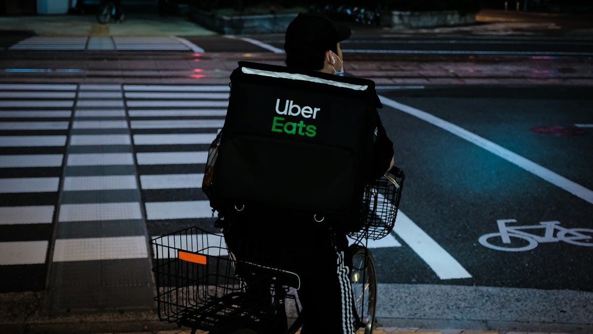 夜の横断歩道でUber Eatsのバッグを背負う自転車の配達員